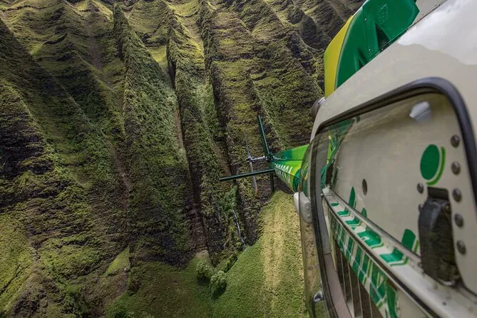 A view past a helicopter door down to green Na Pali ridges