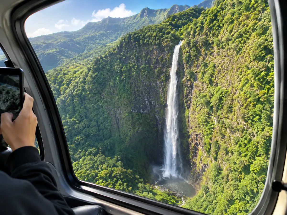Una cascada en un acantilado verde vertical vista a través de la ventanilla de un helicóptero